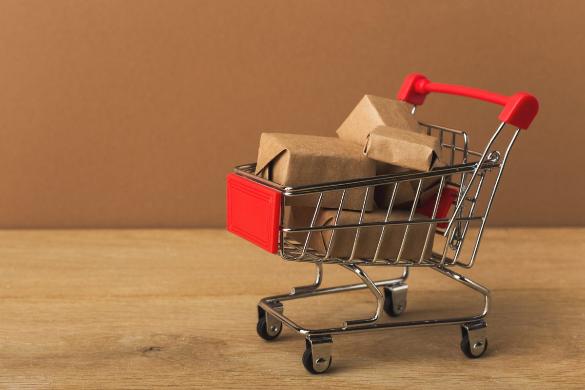 Miniature shopping cart and parcels on brown background,