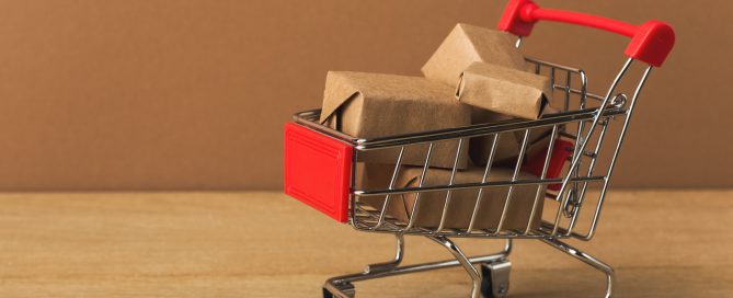 Miniature shopping cart and parcels on brown background,